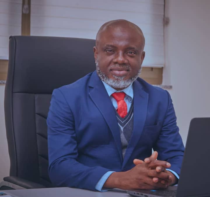 Dr, Bethel in a blue suit and a red tie, sitting at his desk